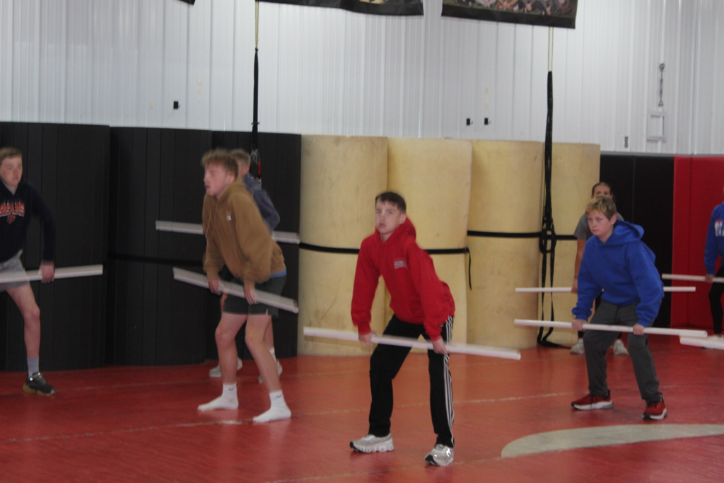 Students practice lifting techniques with PVC pipes during a strength and conditioning session in the wrestling room.