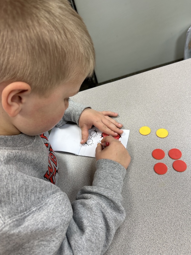 Student colors a ladybug worksheet while sorting red and yellow counting chips at a classroom table.