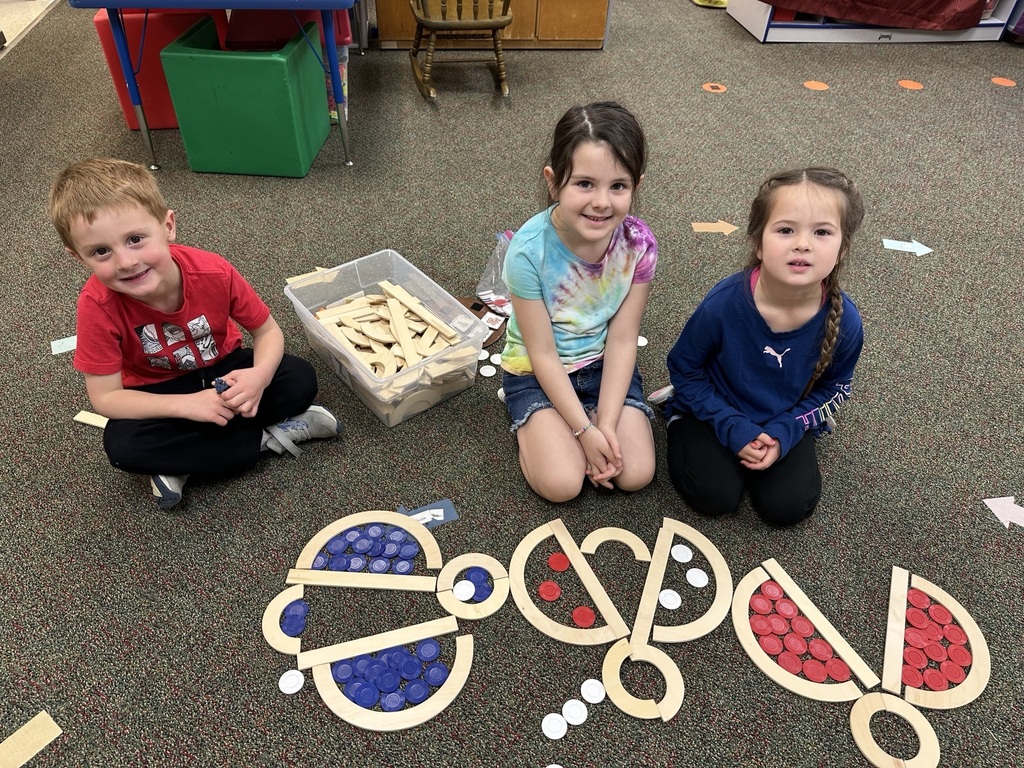 Three students sit beside colorful insect designs made with wooden shapes and counting chips during a classroom activity.