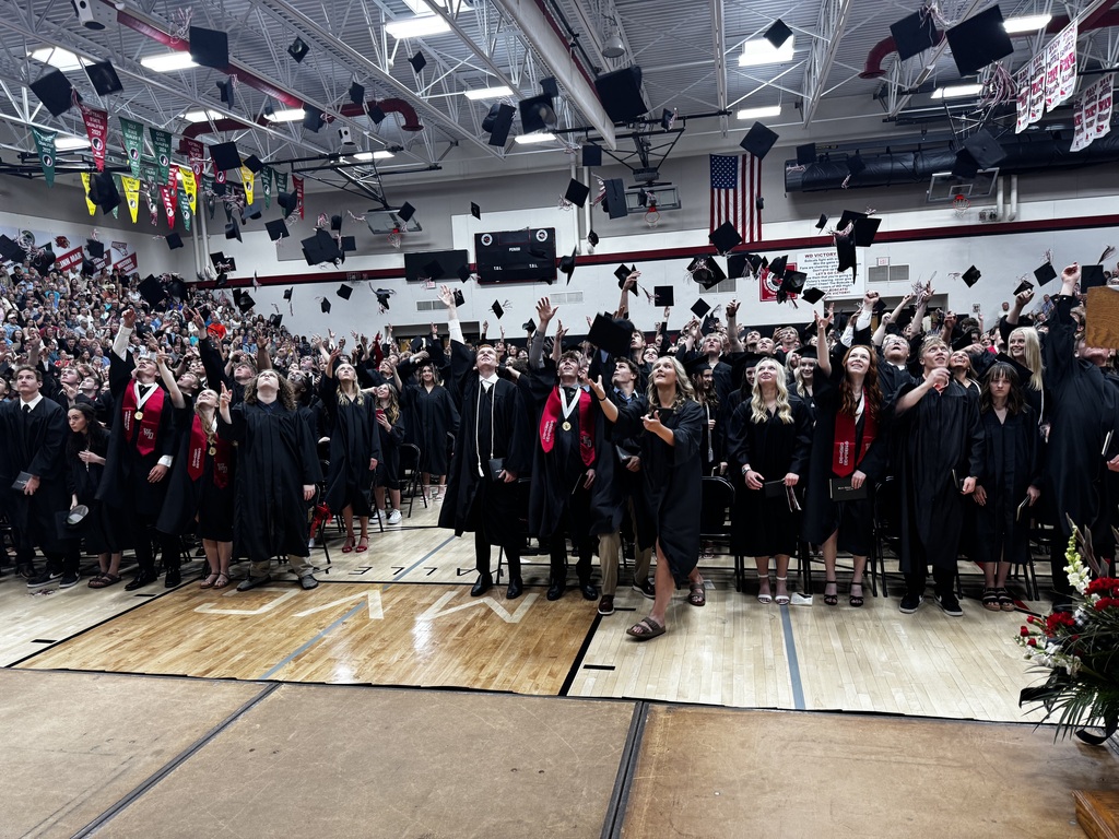Gym full of students throwing their graduation hats.