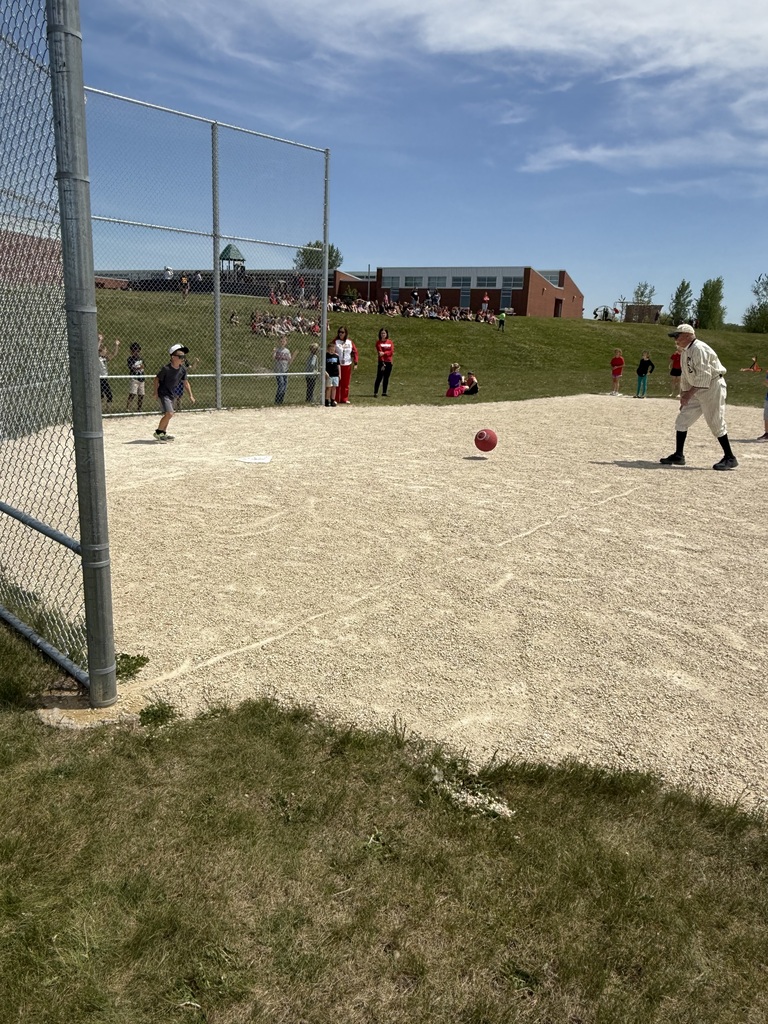 Man pitching kickball to student.