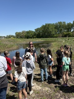 Group of kids learning from teacher near a pond