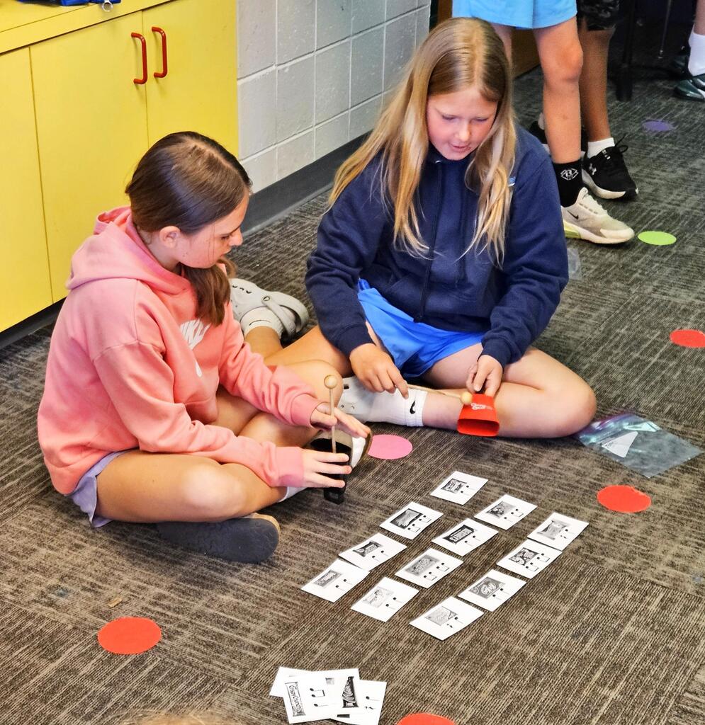 Two students use handbells and music cards while practicing rhythm patterns during music class.