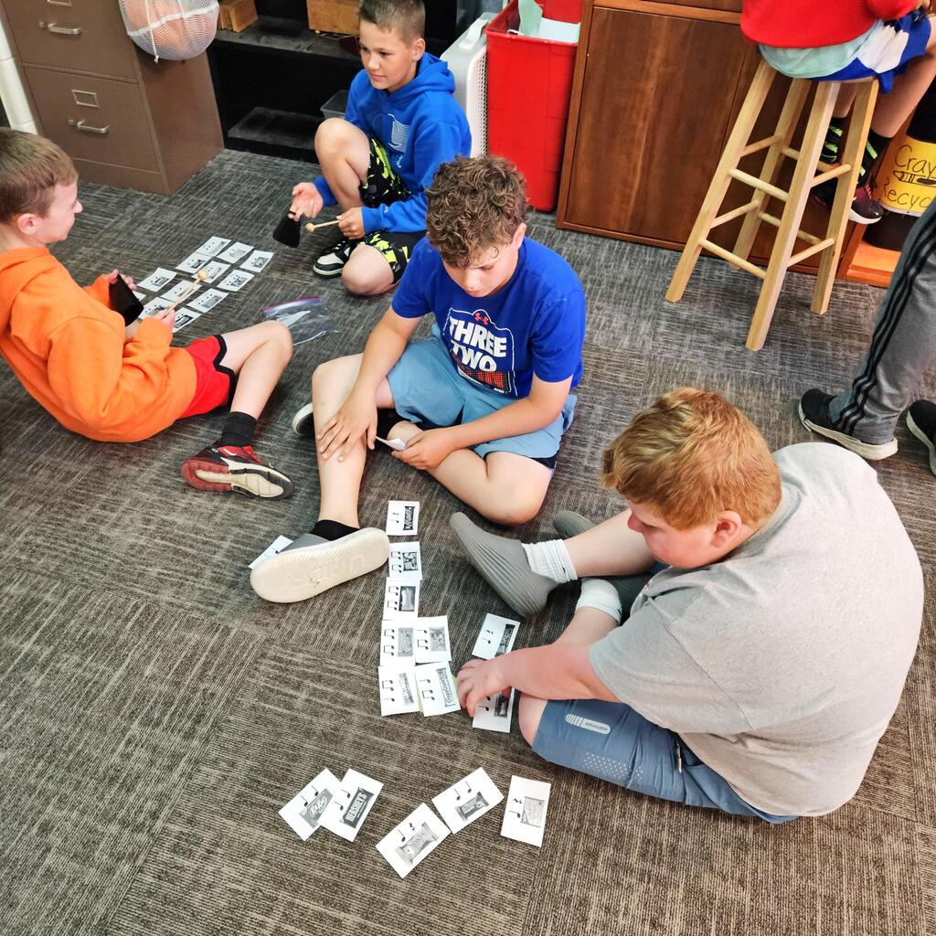 Four students sit on a classroom floor matching music cards while practicing rhythm and note-reading skills.