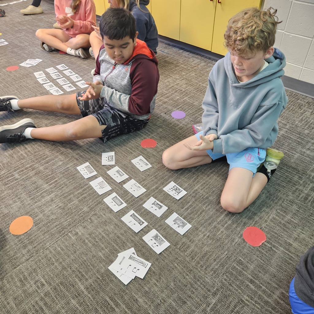 Two students sort music note cards on the classroom floor during a collaborative learning activity.