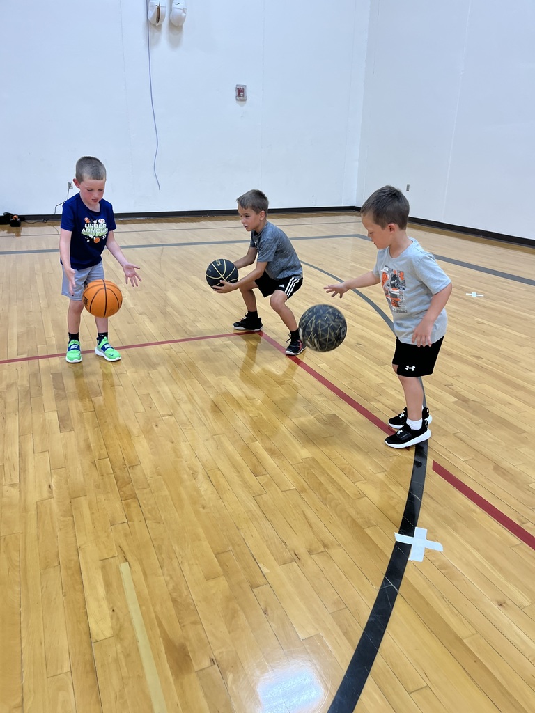 Three young boys practice dribbling basketballs at marked spots on the gym floor during a skills drill.