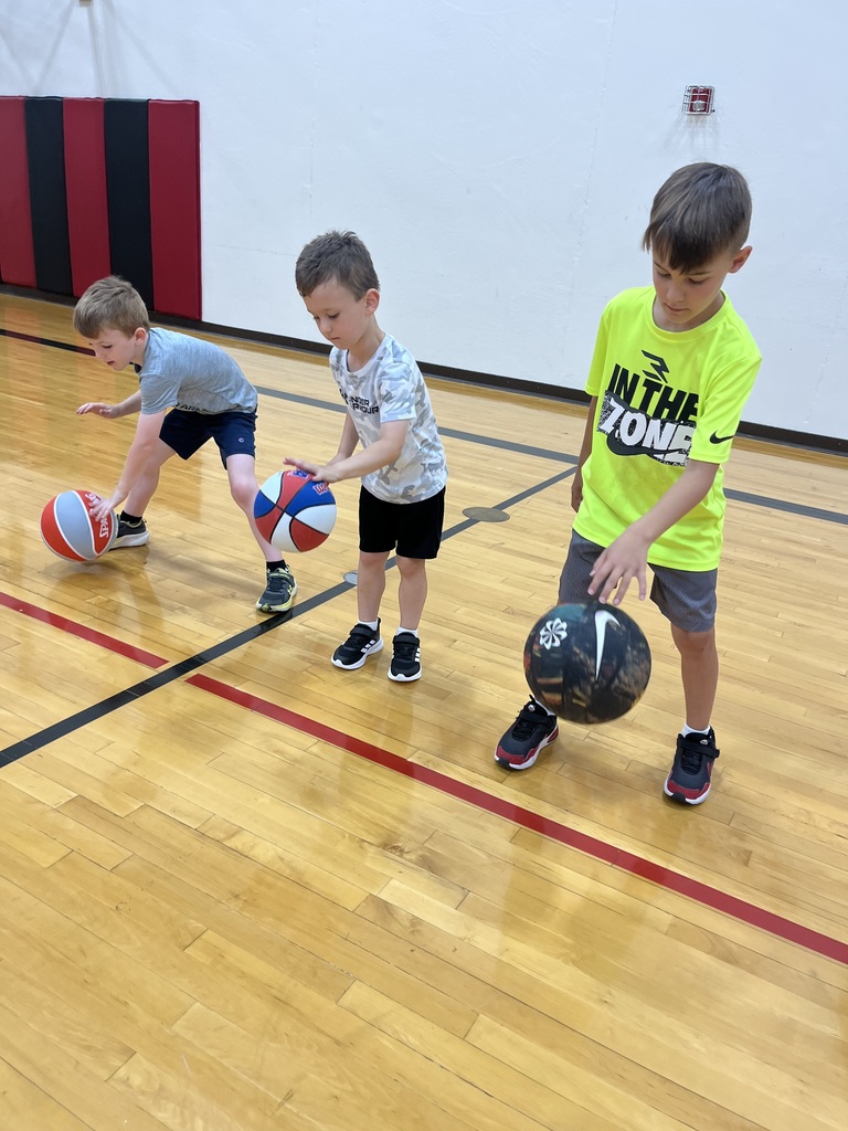 Three boys practice dribbling basketballs in a gym as they work on ball-handling fundamentals.