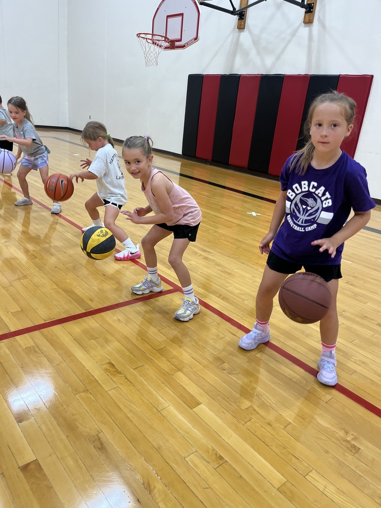 Four young girls practice dribbling basketballs in a gym during a youth basketball camp.