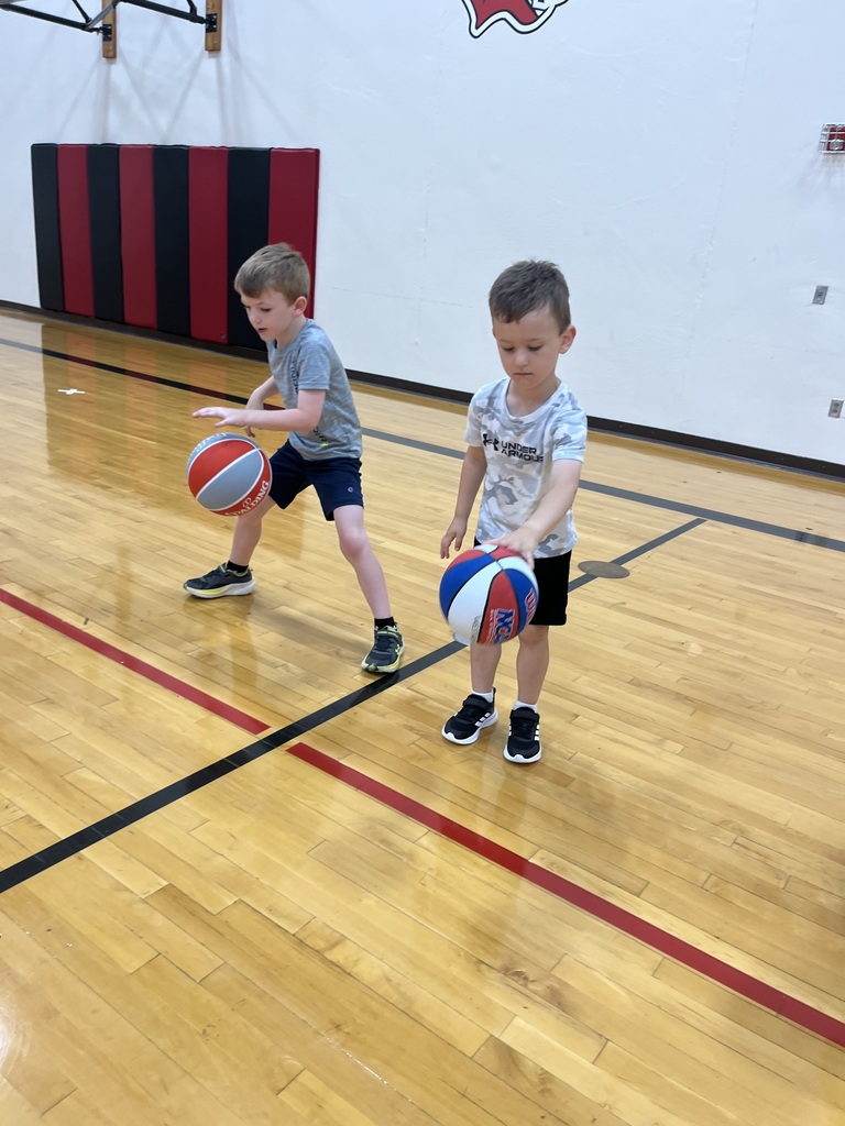 Two young boys practice dribbling basketballs side by side during a youth basketball skills session.