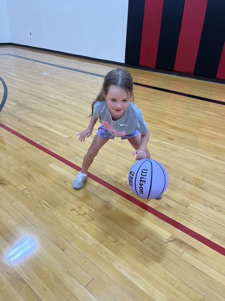 A young girl dribbles a basketball in an athletic stance during a youth basketball skills camp.