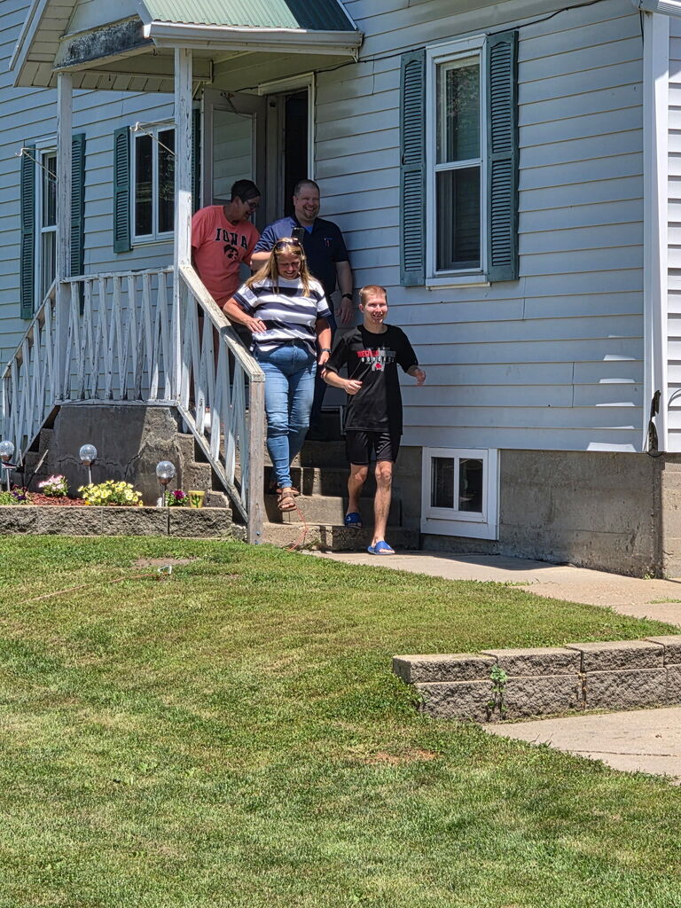 A student and family members step outside their home to greet school staff during a neighborhood visit.