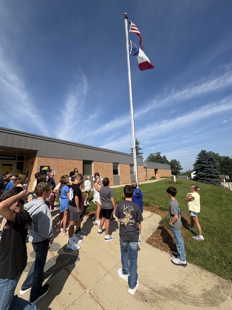 Students gather outside their school and look up at American and Missouri flags flying on a tall flagpole.