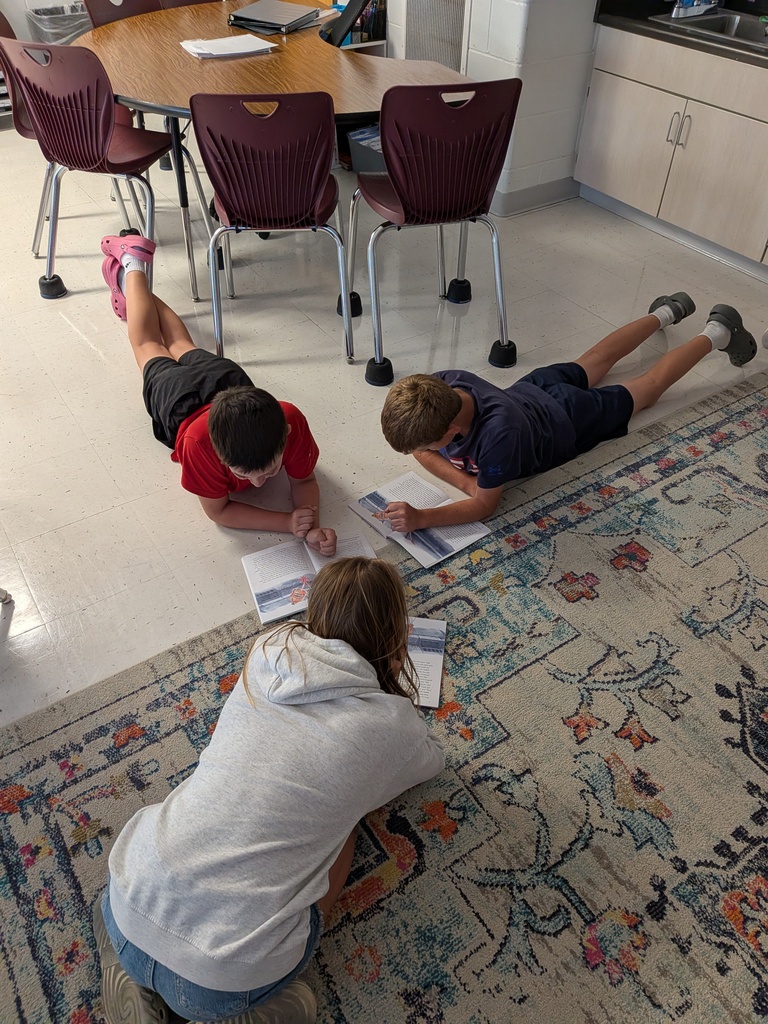 Three students laying on the floor with papers in front of them