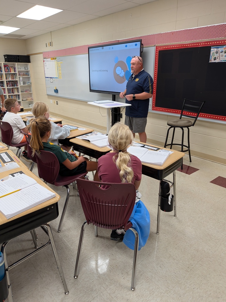 Students sitting at their desks listening to the teacher at the front of the room