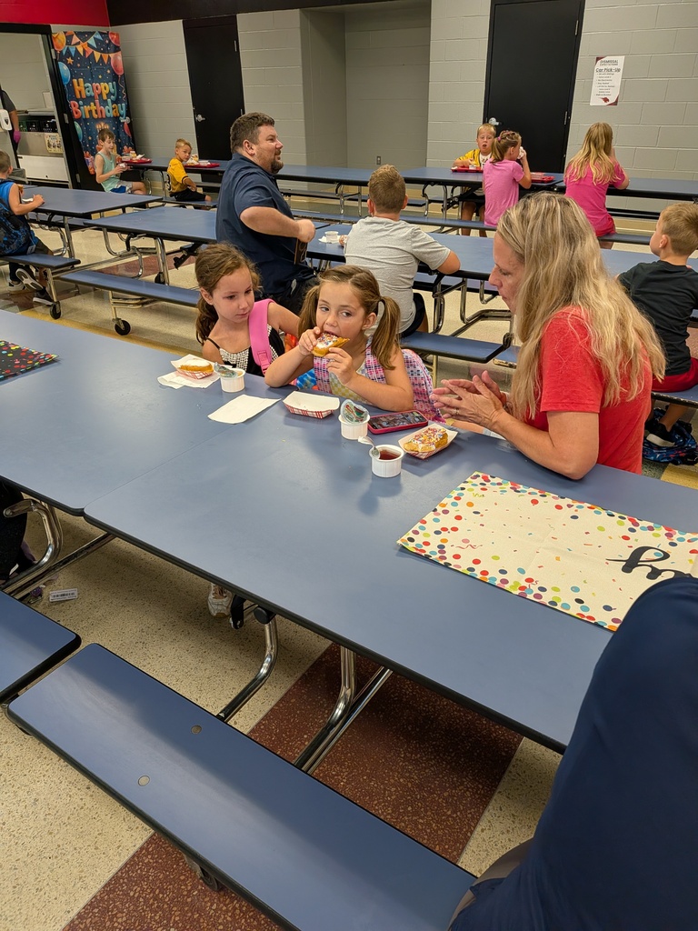 Two students enjoy sprinkled treats while talking with an adult at a cafeteria table during a birthday celebration.