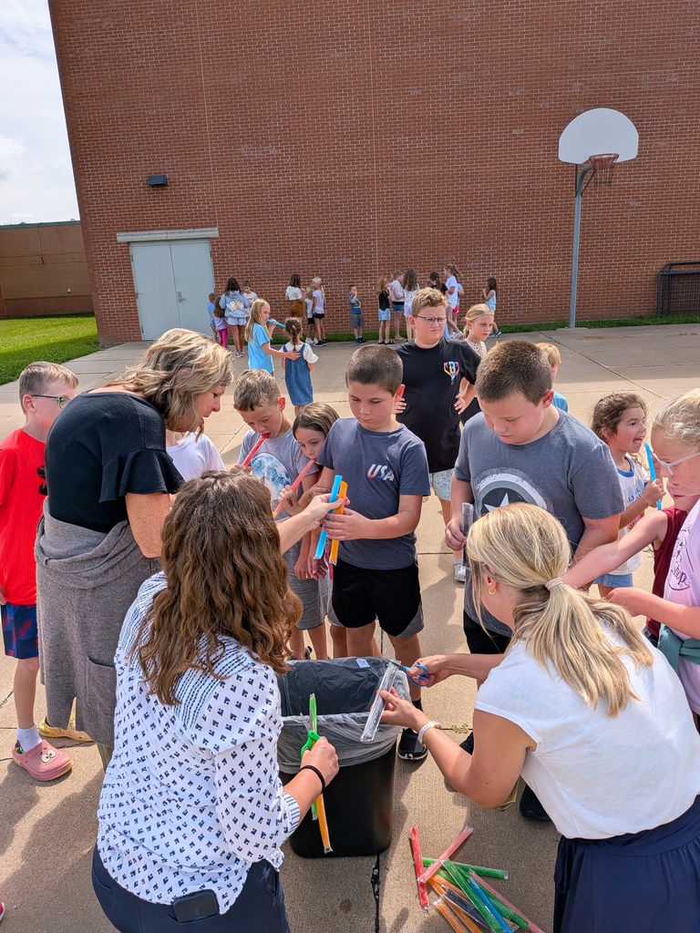 Students gather outdoors as adults distribute colorful frozen treats beside a school building.