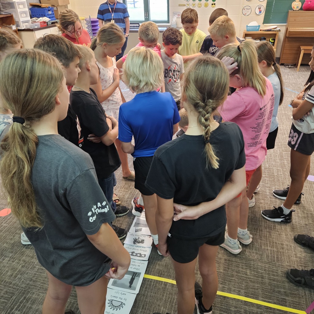 Students gather in a circle around a sequence of illustrated cards arranged on the classroom floor.