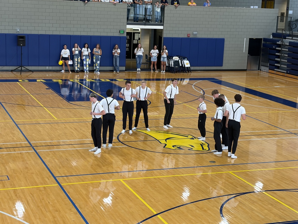 Students in white shirts, black pants, and suspenders gather at center court during a school pep rally.