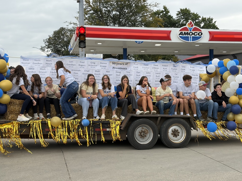 Students ride a blue, gold, and white decorated parade float featuring a display honoring “50 years of Presidents.”