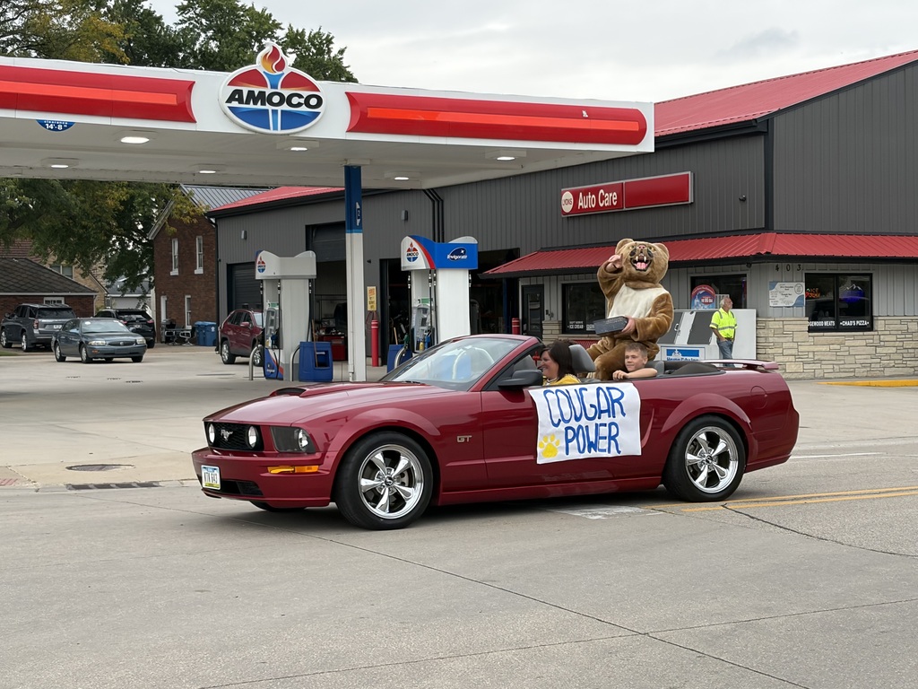 A cougar mascot rides in a red convertible displaying a “Cougar Power” sign during a school parade.