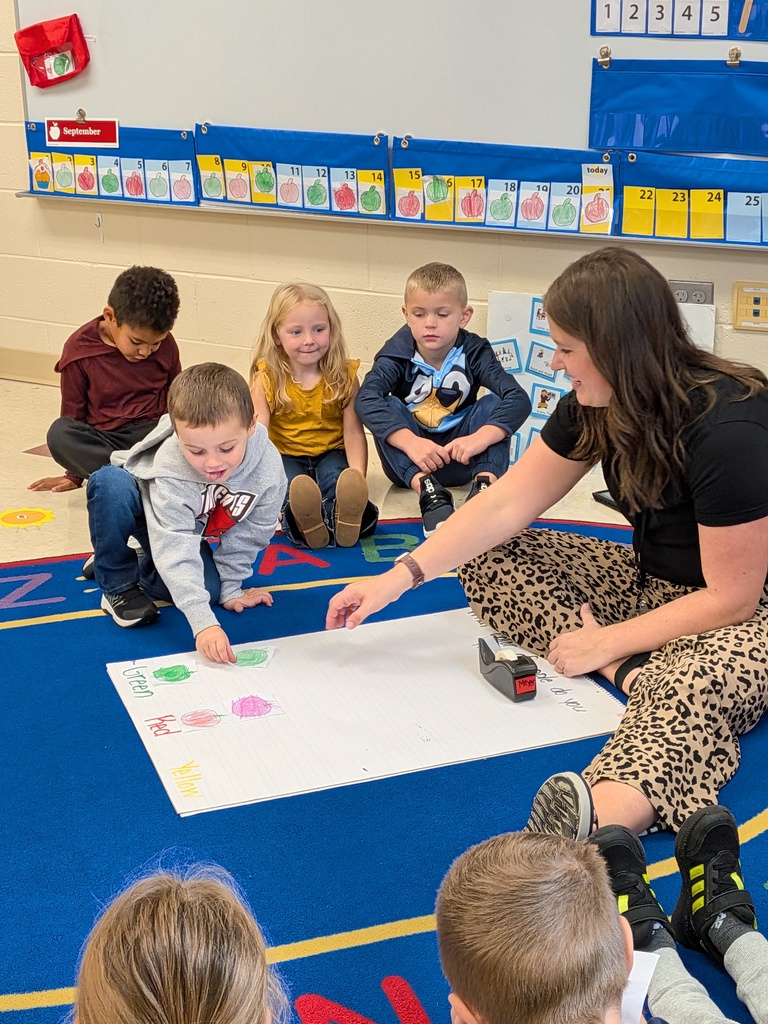 A teacher guides students as they add apple drawings to a floor graph labeled green, red, and yellow.