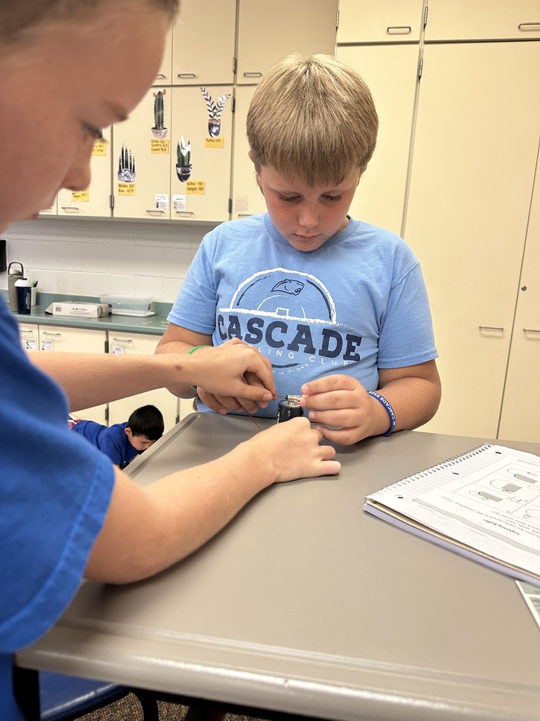 Two students carefully connect wires to a battery while working together on a hands-on electricity lesson.