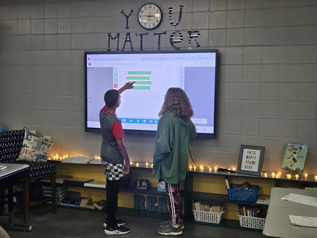 Two students work together at an interactive classroom display, using visual math models to solve a problem.