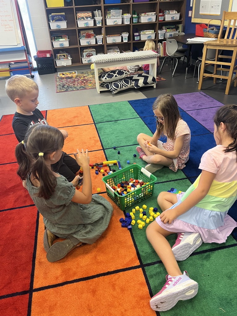 Four students gather on a colorful classroom rug, building and sorting patterns with multicolored math cubes.