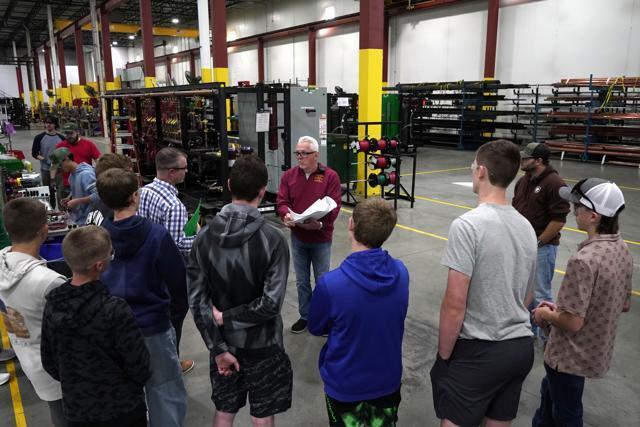 Students standing in a manufacturing plant listening to a man speak.