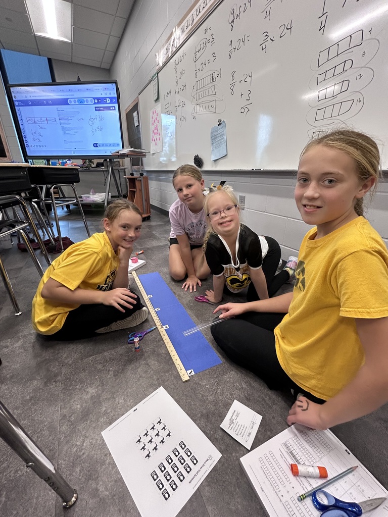 Four girls work together on a hands-on math activity, using rulers and paper strips to explore fractions.