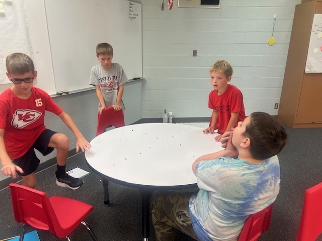 Students playing marbles using pom poms.