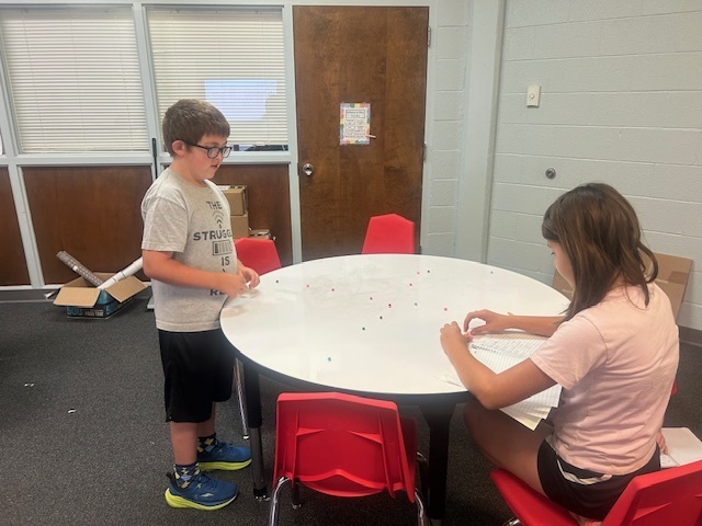 Students playing marbles using pom poms.