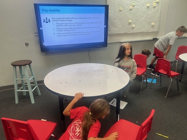 Students playing marbles using pom poms.