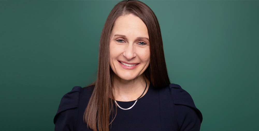 A photo of Laurie Sharp standing against a green background.