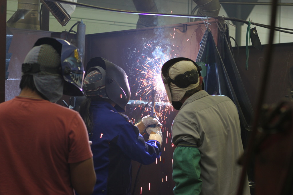 A student welds as another student and the instructor watch.