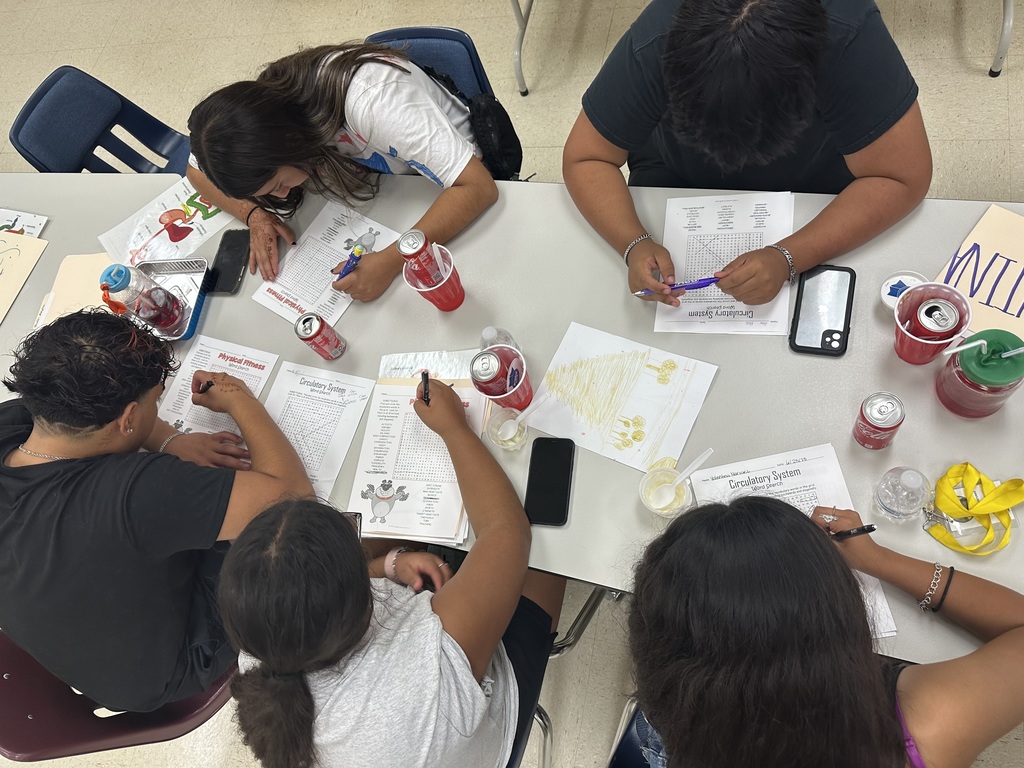 Students finish assignments at a table while enjoying sodas and snacks.