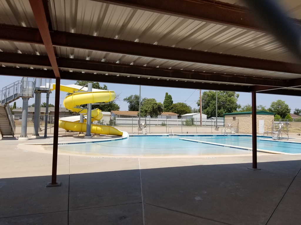 A view of the pool with the yellow slide on the left from the covered sitting area.