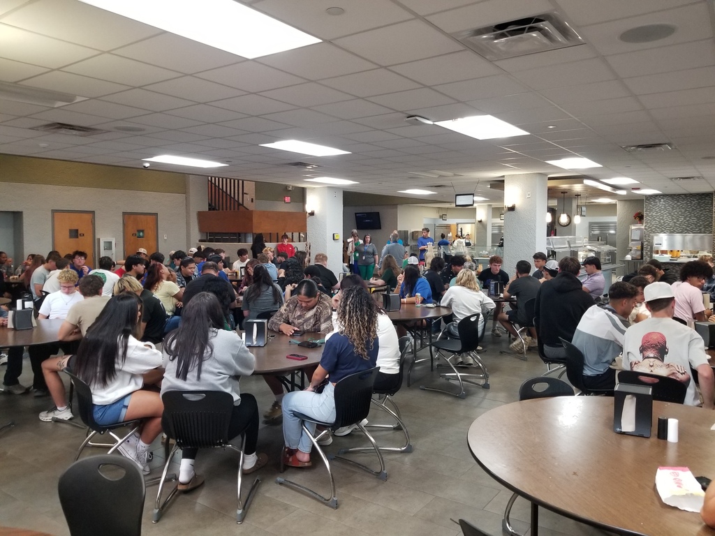 Students sit at round tables in the Cafeteria listening to Mr. Ramon speak.