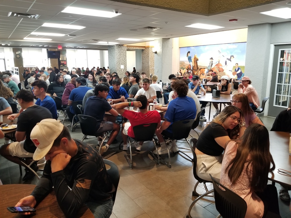 Students sit at round tables in the Cafeteria listening to Mr. Ramon speak.