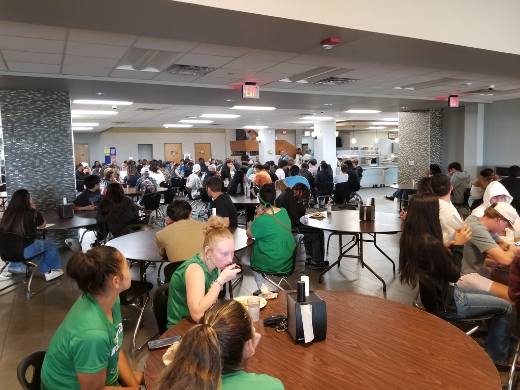 Students sit at round tables in the Cafeteria listening to Mr. Ramon speak.