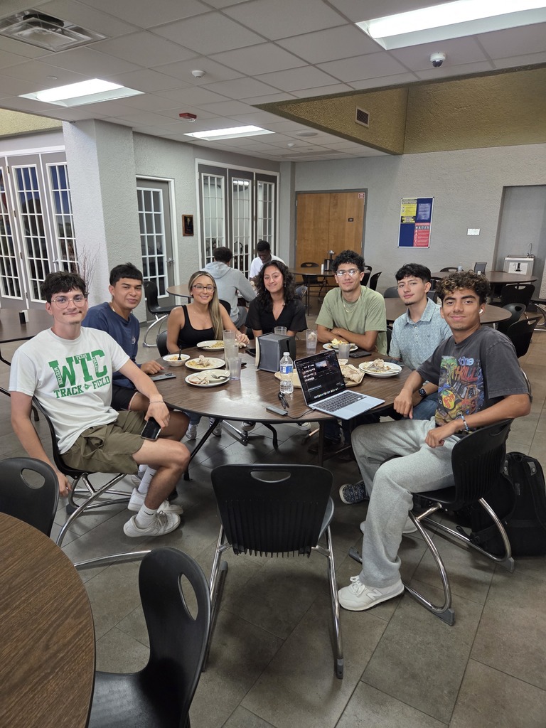 A group of students smile for the camera while eating lunch.