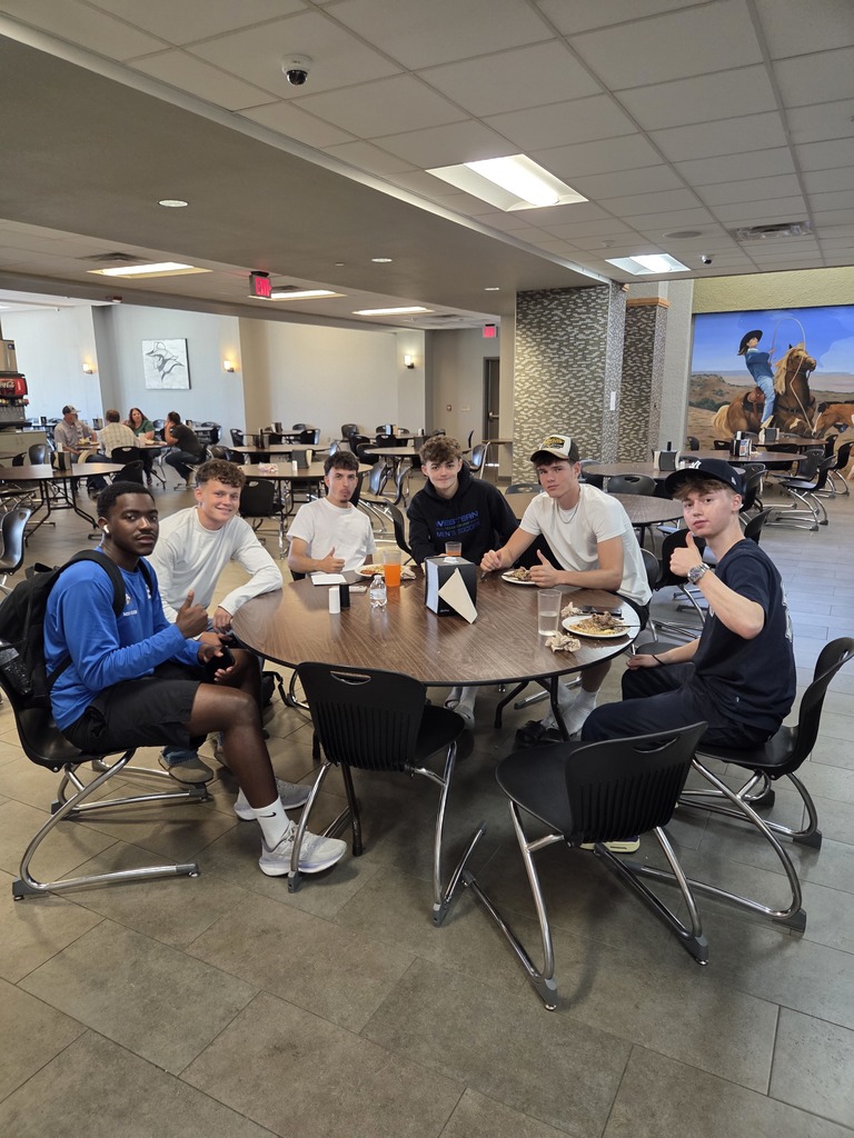 A group of students smile for the camera while eating lunch.