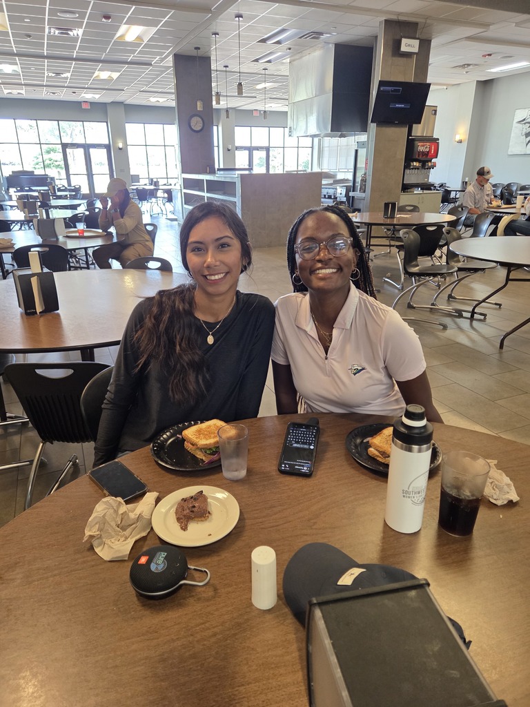 Two women smile for the camera while eating lunch.