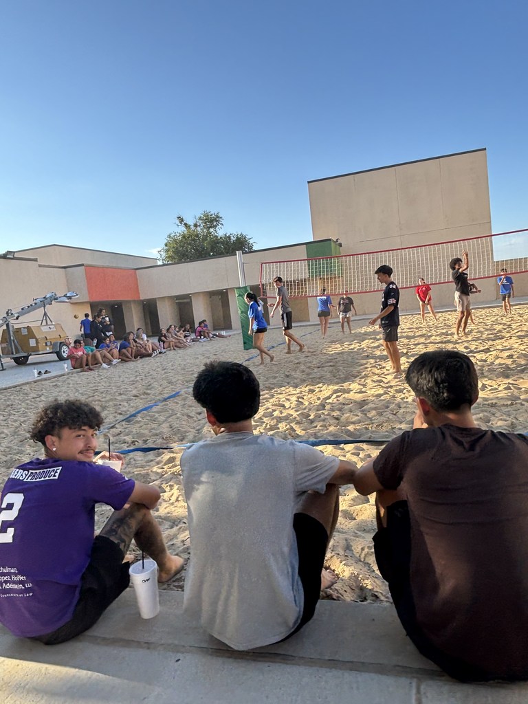 Three students watch the volleyball game as one smiles at the camera.