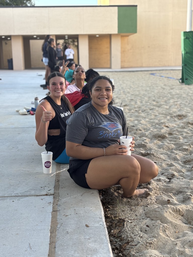 Students smile for the camera sitting on the sideline of the volleyball game.