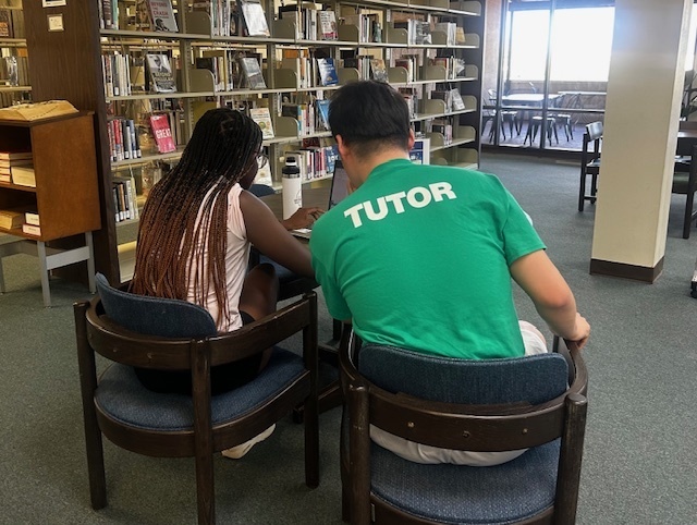A tutor helps a student sitting at a table in the Library.