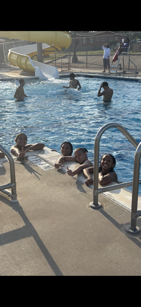 A group of students smile for the camera while hanging on to the side of the pool.