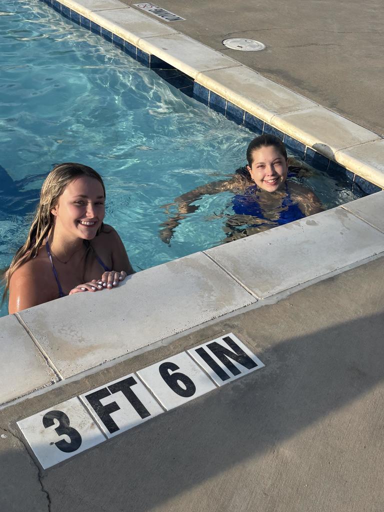Two students smile from the side of the pool.
