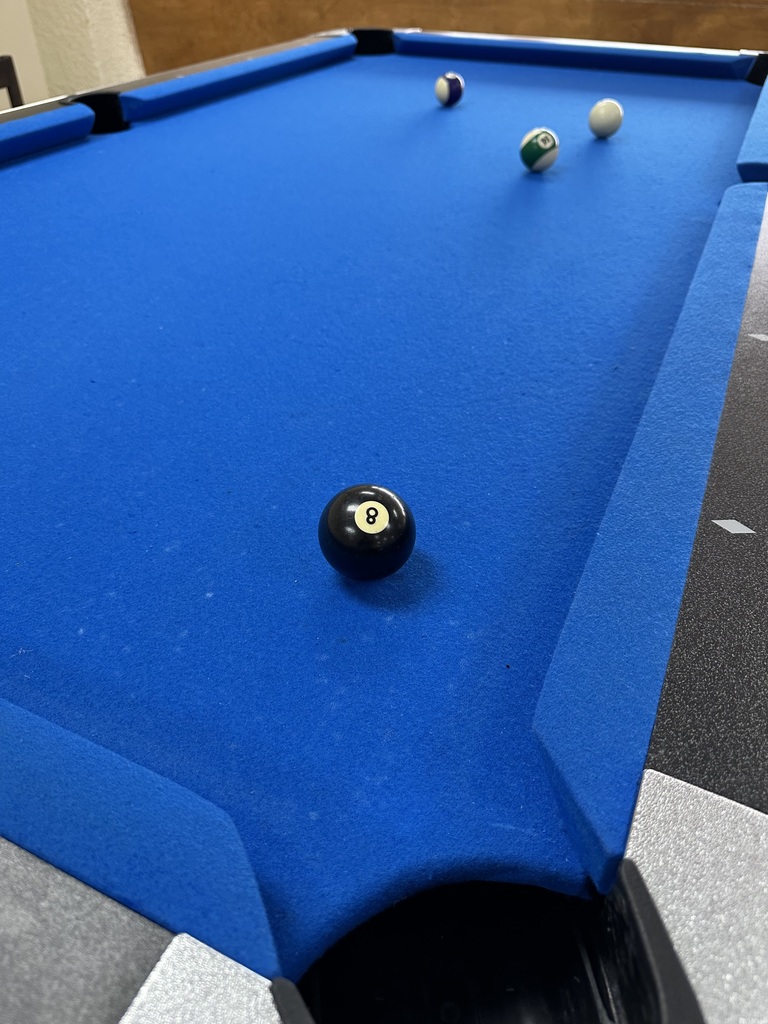 An eight ball sits on a pool table covered in blue felt.