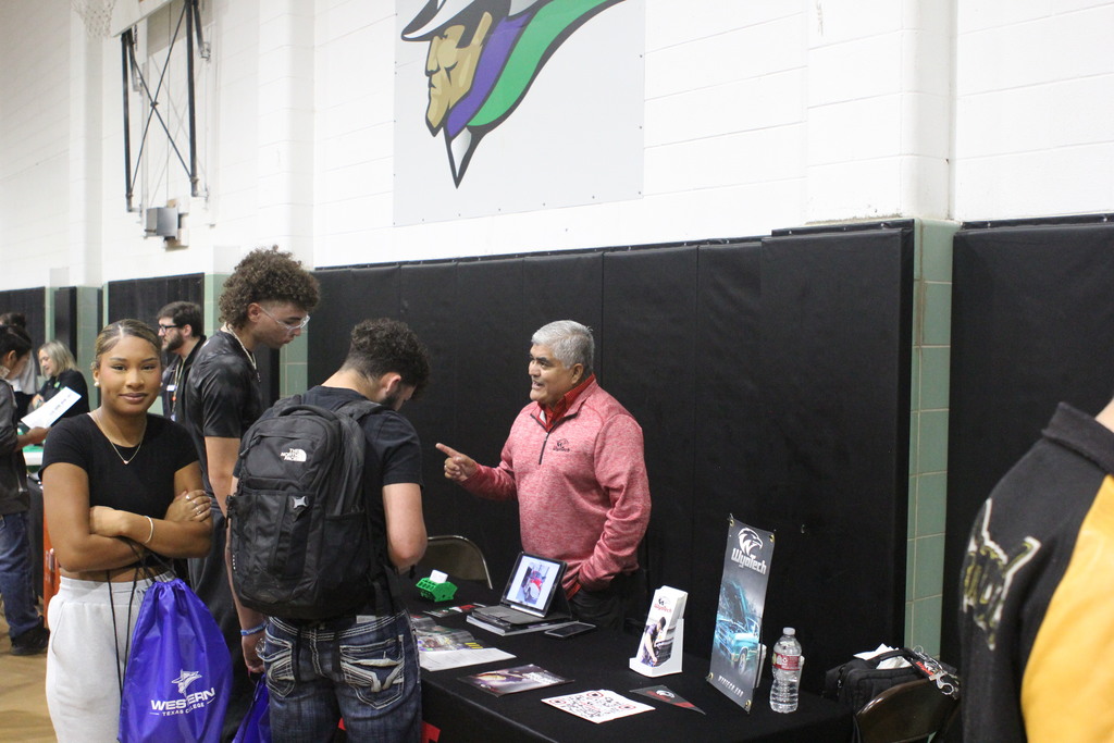 A student with a WTC backpack smiles while students talk with a trade school rep.